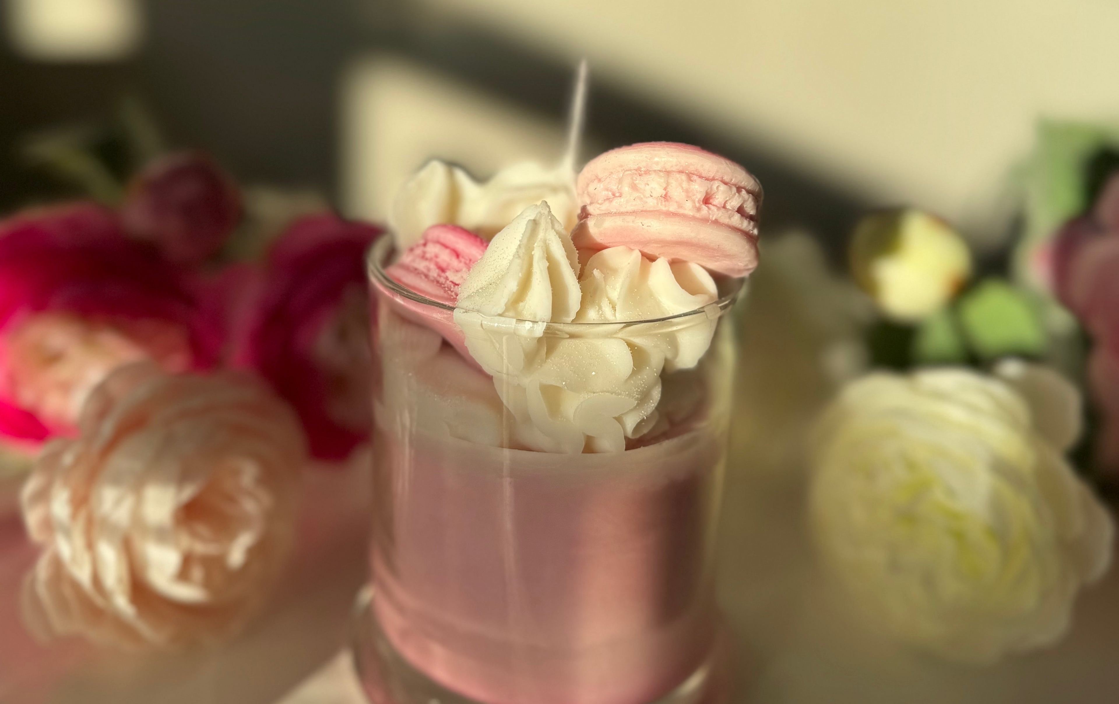 Pink candle with whipped cream and macarons in a glass, surrounded by flowers